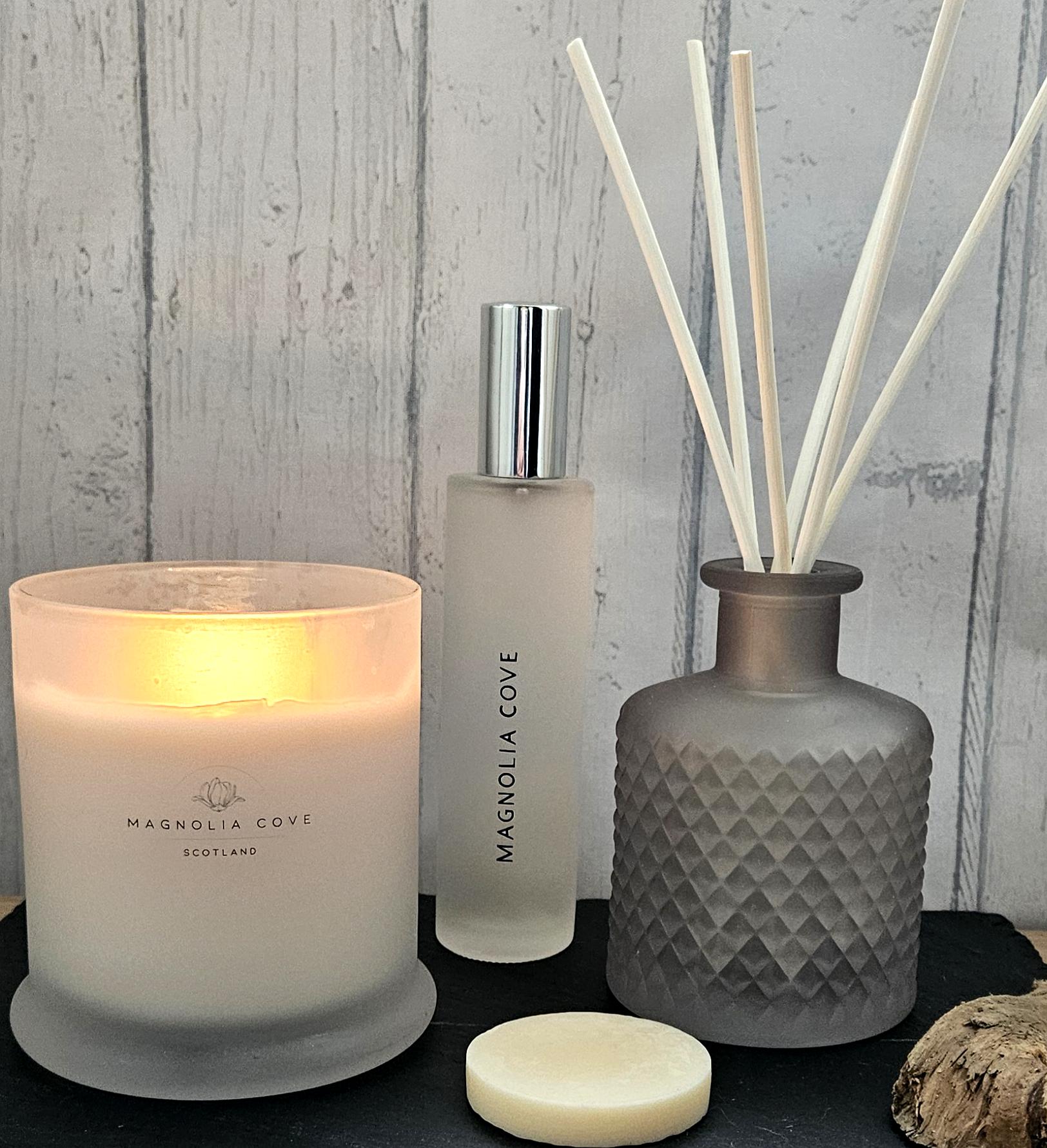 Candle, diffuser, and reed diffuser set with 'Magnolia Cove' branding on a wooden surface.